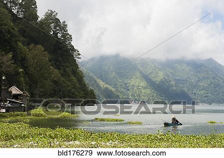 Stock Photo - Fisherman rowing canoe on still rural lake. Fotosearch
