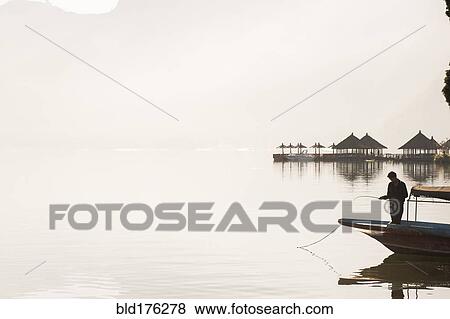 Fisherman standing in boat on still remote lake View Large Photo Image Stock Photo - Fisherman standing in boat on still remote lake. Fotosearch