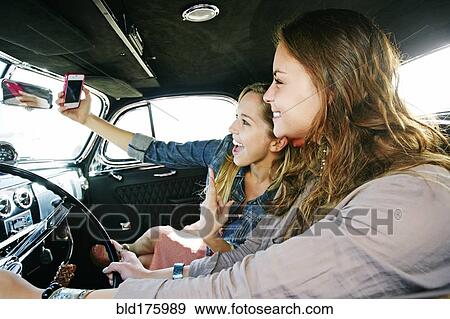 Stock Photo - Friends taking selfie in vintage car. Fotosearch