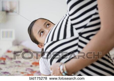 Stock Photo - Girl admiring belly of pregnant mother. Fotosearch