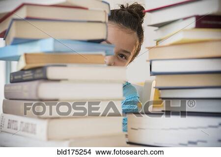 Picture - Girl peeking from behind stacks of books. Fotosearch
