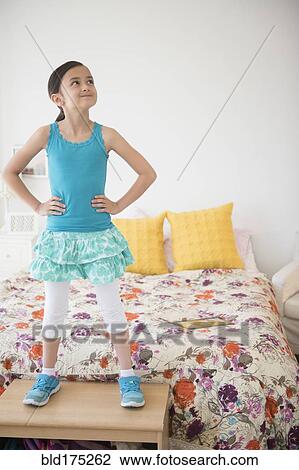 Stock Image - Girl standing on table near bed. Fotosearch