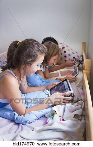 Girls using digital tablets on bed View Large Photo Image Stock Image - Girls using digital tablets on bed. Fotosearch