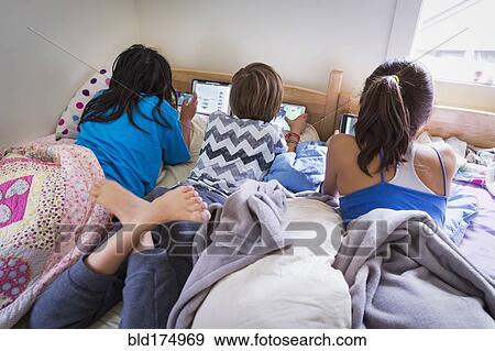Stock Photo - Girls using digital tablets on bed. Fotosearch