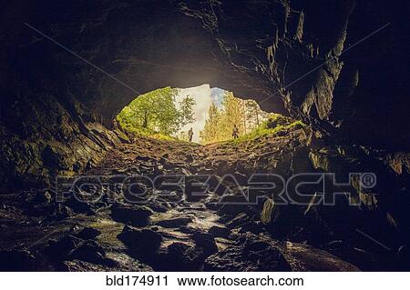 Stock Image - Hikers standing at entrance of cave. Fotosearch