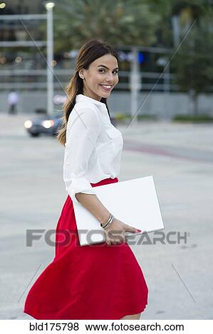 Stock Photo - Hispanic businesswoman carrying laptop outdoors. Fotosearch
