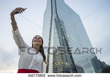 Stock Image - Hispanic businesswoman taking selfie outdoors. Fotosearch