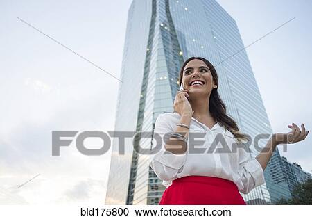 Stock Image - Hispanic businesswoman talking on cell phone outdoors. Fotosearch