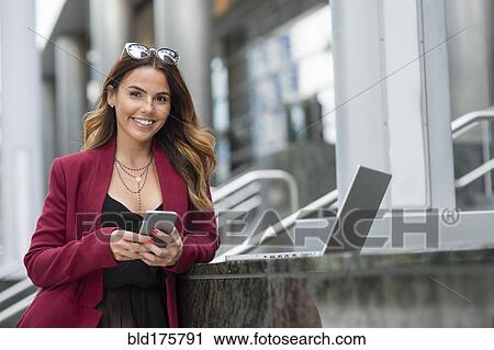 Stock Image - Hispanic businesswoman using cell phone outdoors. Fotosearch