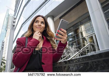 Stock Image - Hispanic businesswoman using cell phone outdoors. Fotosearch