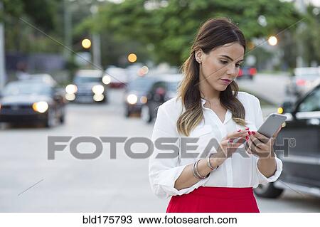 Stock Image - Hispanic businesswoman using cell phone outdoors. Fotosearch