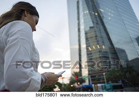 Stock Image - Hispanic businesswoman using cell phone outdoors. Fotosearch