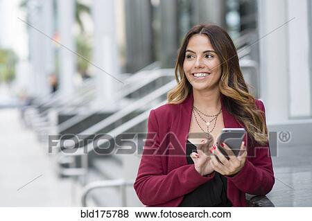 Stock Photo - Hispanic businesswoman using cell phone outdoors. Fotosearch