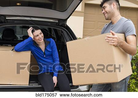Stock Photo - Hispanic couple carrying cardboard boxes near car. Fotosearch