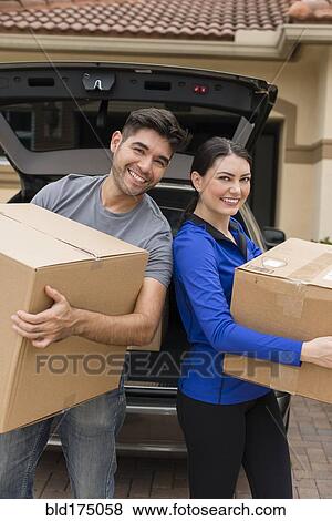 Stock Photo - Hispanic couple carrying cardboard boxes near car. Fotosearch