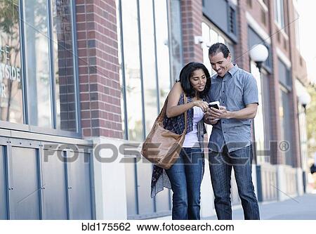 Stock Image - Hispanic couple using cell phone outdoors. Fotosearch