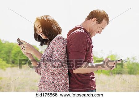 Hispanic couple using cell phones outdoors View Large Photo Image Stock Photograph - Hispanic couple using cell phones outdoors. Fotosearch