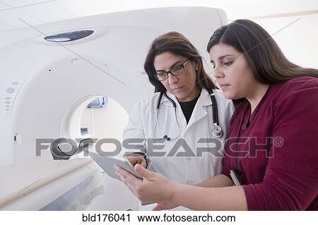 Stock Image - Hispanic doctor and nurse using digital tablet in MRI room. Fotosearch