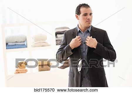 Stock Image - Hispanic man trying on suit in store. Fotosearch