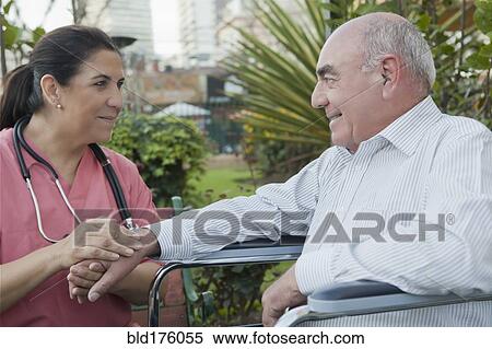 Stock Photography - Hispanic nurse comforting patient in wheelchair. Fotosearch