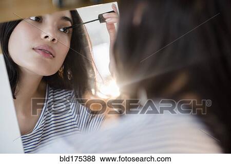 Stock Photo - Hispanic woman applying mascara in mirror. Fotosearch