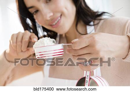 Stock Image - Hispanic woman measuring flour. Fotosearch
