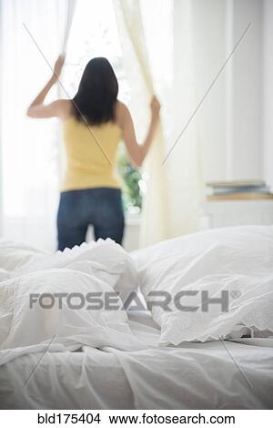 Picture - Hispanic woman opening curtains. Fotosearch