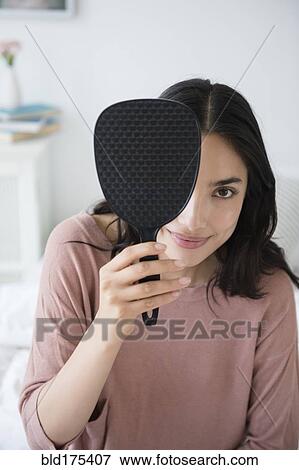 Stock Photo - Hispanic woman peeking out from behind hand mirror. Fotosearch