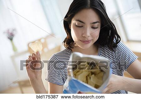 Stock Photo - Hispanic woman reading ingredients on bag of potato chips. Fotosearch