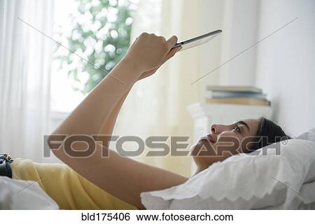 Stock Photograph - Hispanic woman using digital tablet in bed. Fotosearch