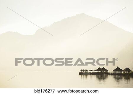 Stock Photo - Huts reflecting in still remote lake under mountains. Fotosearch