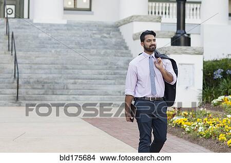 Picture - Indian businessman carrying digital tablet on sidewalk. Fotosearch