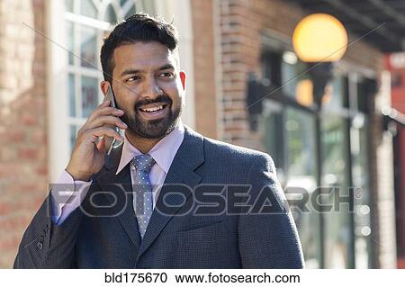 Stock Image - Indian businessman talking on cell phone in city. Fotosearch