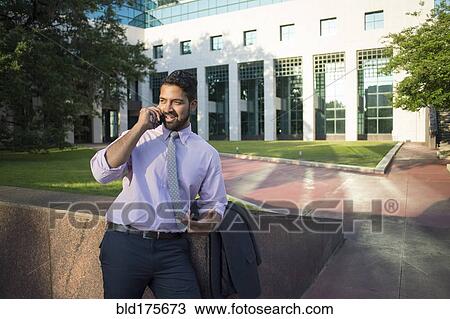 Stock Image - Indian businessman talking on cell phone outside office building. Fotosearch