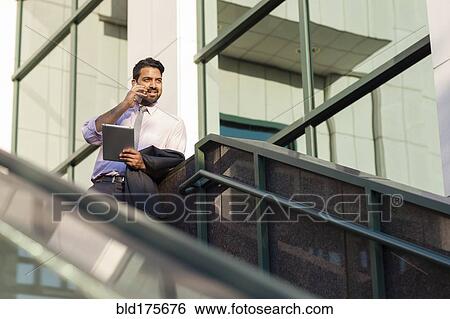Stock Photograph - Indian businessman talking on cell phone on steps. Fotosearch