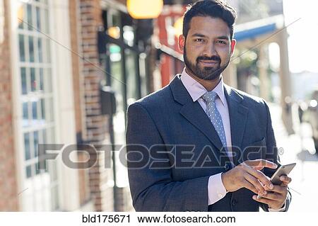 Stock Image - Indian businessman using cell phone in city. Fotosearch
