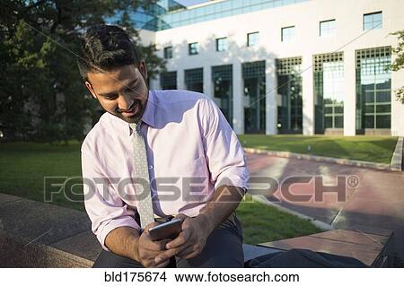 Indian businessman using cell phone outside office building View Large Photo Image Picture - Indian businessman using cell phone outside office building. Fotosearch