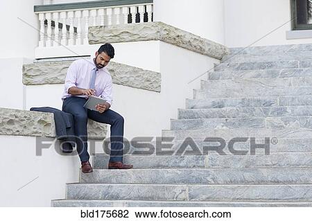 Stock Image - Indian businessman using digital tablet on steps. Fotosearch