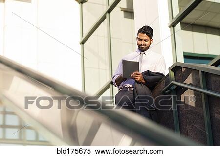Stock Photography - Indian businessman using digital tablet on steps. Fotosearch