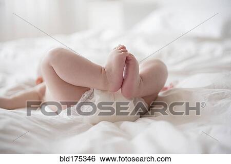 Stock Photograph - Legs of Caucasian baby girl laying on bed. Fotosearch