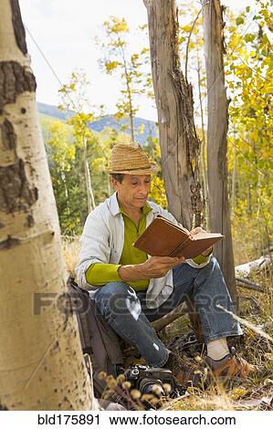Stock Image - Man reading book in autumn forest. Fotosearch