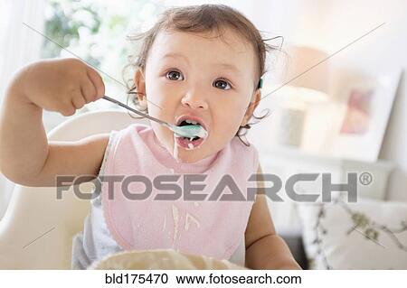 Stock Image - Mixed race baby girl eating yogurt. Fotosearch