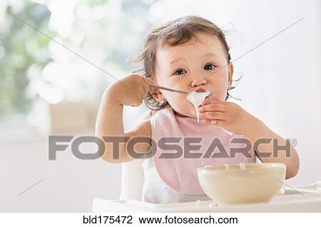 Stock Image - Mixed race baby girl eating yogurt. Fotosearch