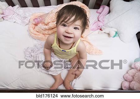 Picture - Mixed race baby girl sitting in crib. Fotosearch