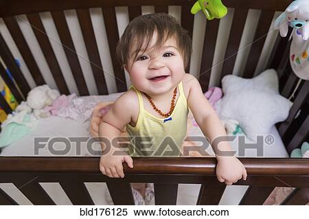 Stock Photography - Mixed race baby girl standing in crib. Fotosearch