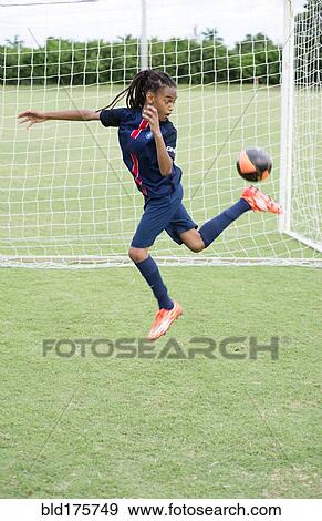 Stock Photo - Mixed race boy kicking soccer ball on field. Fotosearch