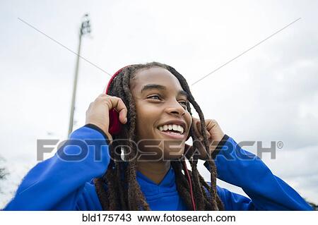 Stock Image - Mixed race boy listening to headphones outdoors. Fotosearch