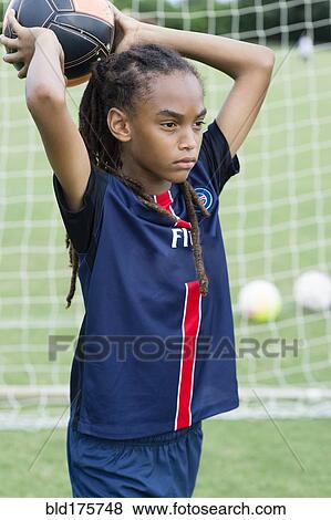Stock Photo - Mixed race boy throwing soccer ball on field. Fotosearch