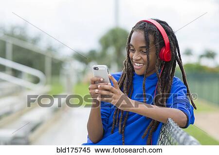 Stock Photography - Mixed race boy using cell phone on bleachers. Fotosearch