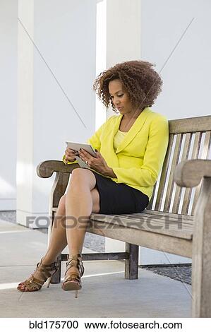 Stock Image - Mixed race businesswoman using digital tablet on bench. Fotosearch